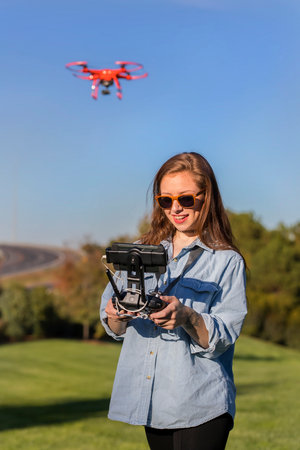 A beautiful young woman skillfully pilots a drone under the bright sun, practicing maneuvers with...