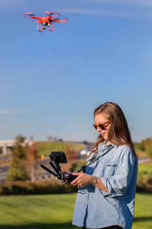 A beautiful young woman skillfully pilots a drone under the bright sun, practicing maneuvers with...