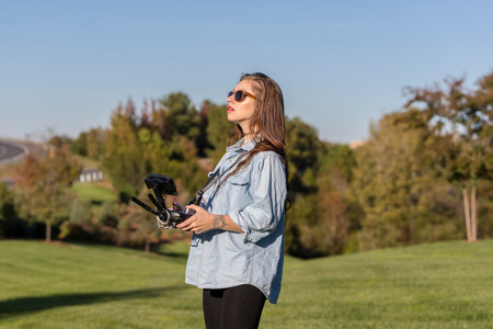 A beautiful young woman skillfully pilots a drone under the bright sun, practicing maneuvers with...