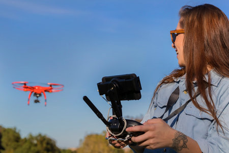 A beautiful young woman skillfully pilots a drone under the bright sun, practicing maneuvers with...