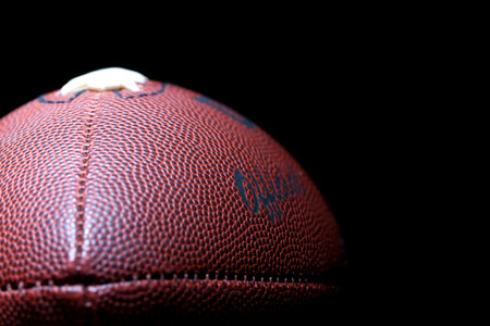 A close-up of an American football reveals detailed leather texture and precise stitching,...