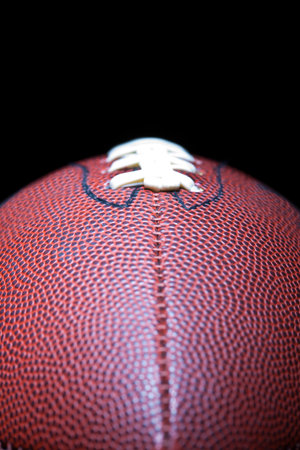 A close-up of an American football reveals detailed leather texture and precise stitching, photographed in a studio against a black background, highlighting its craftsmanship and iconic design.の写真素材