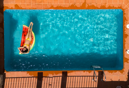 Captivating Spanish beauty luxuriates in European sun on pool float, a serene moment from above.