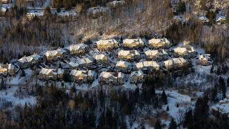 An aerial view showcases a small Canadian town blanketed in fresh snow. Rooftops and streets glisten white, while evergreens stand tall.の写真素材