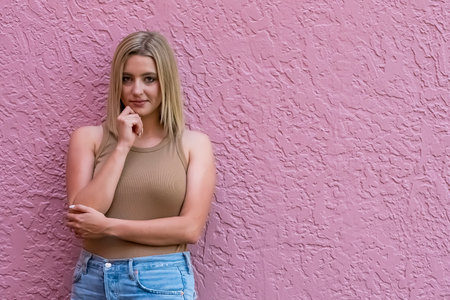 A blonde woman poses against a pink wall, her hair glowing in the sunlight.の写真素材