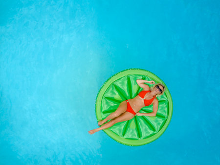 A gorgeous blonde bikini model relaxes by a Caribbean pool, soaking up the sun and gentle Tradewinds. She enjoys the warmth, tranquility, and tropical vibes while perfecting her golden tan.の写真素材