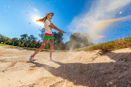 A young woman tees off on fairways, smiling in sunlight, confident swing flowing with the breeze, enjoying every graceful moment of her golf round.の写真素材
