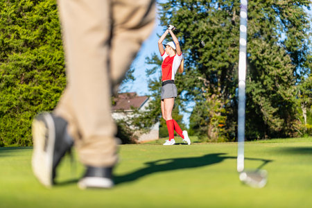 A young, beautiful woman savors warm spring air as she tees off on lush fairways, smiling in sunlight, confident swing flowing with the breeze, enjoying every graceful moment of her golf round.の写真素材