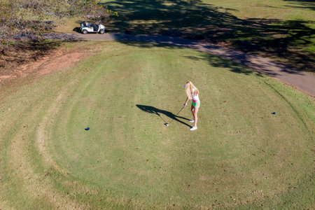 A young, beautiful woman savors warm spring air as she tees off on lush fairways, smiling in sunlight, confident swing flowing with the breeze, enjoying every graceful moment of her golf round.の写真素材