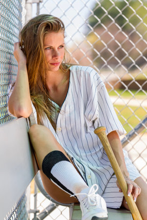 Young woman in baseball gear poses confidently on a sunlit diamond, blue skies above, fresh grass underfoot, capturing athletic grace, youthful energy and seasonal joyの写真素材