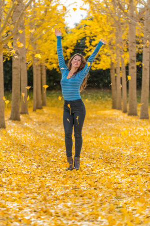A brunette model stands amidst golden autumn leaves, basking in the crisp fall air, her beauty...