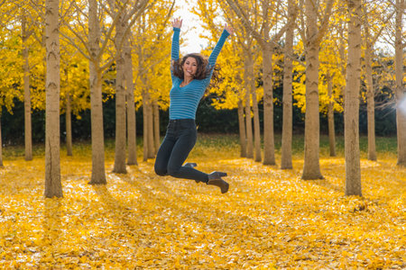 A brunette model stands amidst golden autumn leaves, basking in the crisp fall air, her beauty...