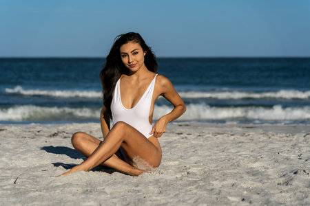 A stunning mixed-race bikini model relaxes on a sunny beach, her glowing skin kissed by the sun. She enjoys the refreshing waves, her confident pose radiating elegance and beauty against the ocean backdrop.の写真素材