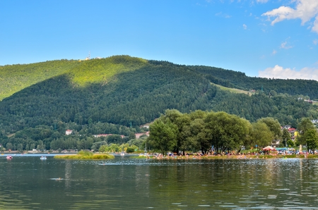 MIEDZYBRODZIE ZYWIECKIE, POLAND - AUGUST 5, 2017: Tourists on the beach at the Miedzybrodzkie lake under the mountain of Zar.のeditorial素材
