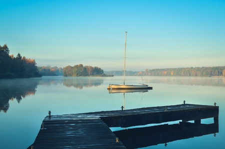 Morning autumn landscape. Wooden pier and boat on a beautiful lake.の写真素材