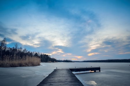 Evening winter landscape. Wooden pier over a beautiful frozen lake.の写真素材