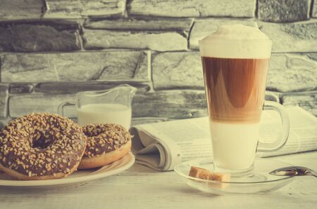 Conceptual delicious sweet breakfast in vintage style. Latte macchiato coffee  with sweet donuts with a hole and morning newspaper.の写真素材