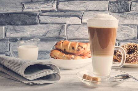 Conceptual delicious sweet breakfast. Latte macchiato coffee  with sweet donuts with a hole and morning newspaper.の写真素材