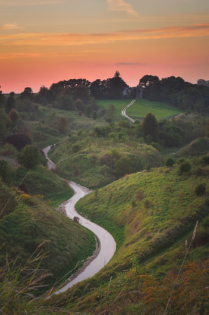 Beautiful evening landscape. The road between green hills at sunset.
