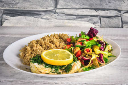 Fresh delicious vegetarian lunch. Fish with lettuce and quinoa on white plates in the kitchen.の写真素材