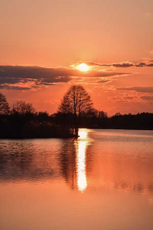 Beautiful sunrise over a Polish lake. Reflection of trees and sun in the water.の写真素材