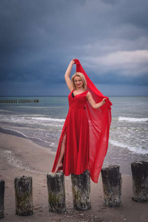 Interesting holiday seaside concept. Beautiful woman in a red dress on the seashore.の写真素材