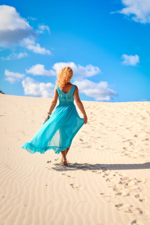Beautiful blonde woman on hot sand with blue sky in the background. Photo taken on the shifting dunes over the Baltic Sea in Åeba, Poland. Photo with a shallow depth of field with blurred background.の写真素材