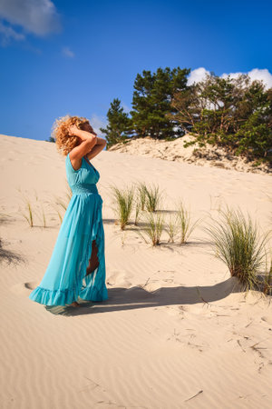Beautiful blonde woman on hot sand with blue sky in the background. Photo taken on the shifting dunes over the Baltic Sea in Åeba, Poland. Photo with a shallow depth of field with blurred background.の写真素材