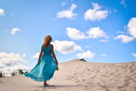Beautiful blonde woman on hot sand with blue sky in the background. Photo taken on the shifting dunes over the Baltic Sea in Åeba, Poland. Photo with a shallow depth of field with blurred background.の写真素材