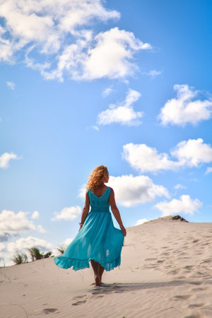 Beautiful blonde woman on hot sand with blue sky in the background. Photo taken on the shifting dunes over the Baltic Sea in Leba, Poland. Photo with a shallow depth of field with blurred background.の写真素材