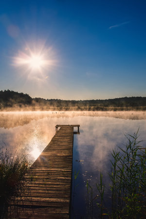 Beautiful summer morning landscape. Wooden pier on the lake shore in the misty morning scenery. Photo taken in Michala Gora, Poland.の写真素材