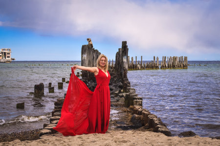 Interesting holiday concept with a blonde-haired woman on the beach. Beautiful woman in a red dress on the shores of the Baltic Sea in Gdynia, Poland.の写真素材