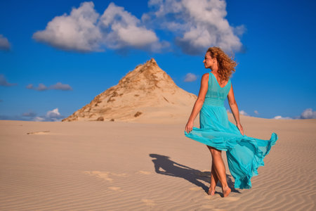 Beautiful blonde woman on hot sand with blue sky in the background. Photo taken on the shifting dunes over the Baltic Sea in Leba, Poland. Photo with a shallow depth of field with blurred background.の写真素材