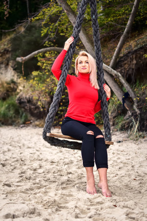 Session of a blonde-haired woman on a Polish beach. Girl on a swing on a sandy beach in Gdynia, Poland. Photo with a shallow depth of field.の写真素材
