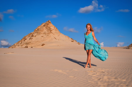 Beautiful blonde woman on hot sand with blue sky in the background. Photo taken on the shifting dunes over the Baltic Sea in Leba, Poland. Photo with a shallow depth of field with blurred background.の写真素材