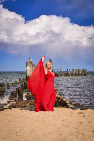 Interesting holiday concept with a blonde-haired woman on the beach. Beautiful woman in a red dress on the shores of the Baltic Sea in Gdynia, Poland.の写真素材