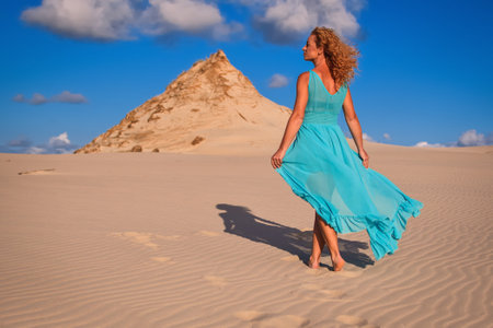 Beautiful blonde woman on hot sand with blue sky in the background. Photo taken on the shifting dunes over the Baltic Sea in Leba, Poland. Photo with a shallow depth of field with blurred background.の写真素材
