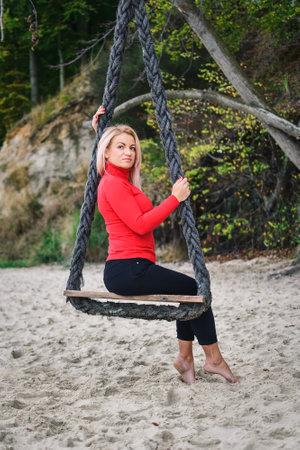 Session of a blonde-haired woman on a Polish beach. Girl on a swing on a sandy beach in Gdynia, Poland. Photo with a shallow depth of field.の写真素材