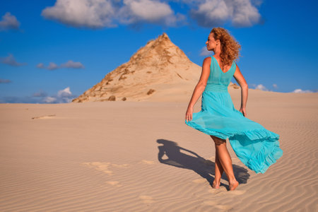 Beautiful blonde woman on hot sand with blue sky in the background. Photo taken on the shifting dunes over the Baltic Sea in Leba, Poland. Photo with a shallow depth of field with blurred background.の写真素材