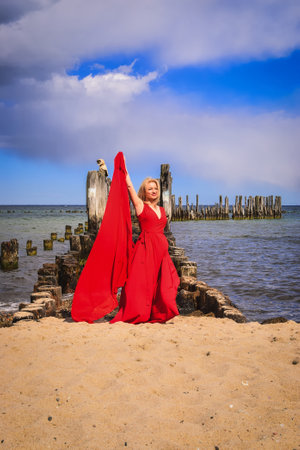 Interesting holiday concept with a blonde-haired woman on the beach. Beautiful woman in a red dress on the shores of the Baltic Sea in Gdynia, Poland.の写真素材