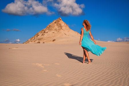 Beautiful blonde woman on hot sand with blue sky in the background. Photo taken on the shifting dunes over the Baltic Sea in Leba, Poland. Photo with a shallow depth of field with blurred background.の写真素材