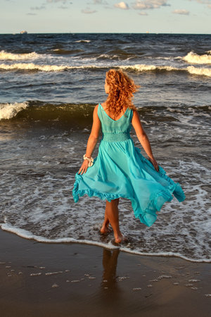 Beautiful blonde haired woman on the beach. Girl in a blue dress at the Polish seaside. Photo taken with a shallow depth of field.の写真素材