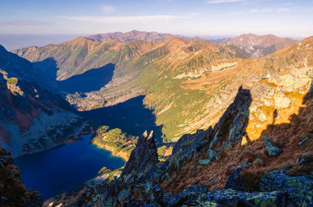 Mountain landscape with lake in the valley. Silhouette of hiker on a steep hillside in Tatra mountains. Photo taken in Szpiglasowy Wierch Peak in Tatra Mountains, Poland.の写真素材