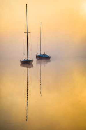 Minimalist morning landscape over a misty lake. Boats reflecting in the water at Lake Paprocany in Tychy, Poland.の写真素材