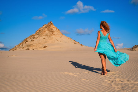 Beautiful blonde woman on hot sand with blue sky in the background. Photo taken on the shifting dunes over the Baltic Sea in Leba, Poland. Photo with a shallow depth of field with blurred background.の写真素材