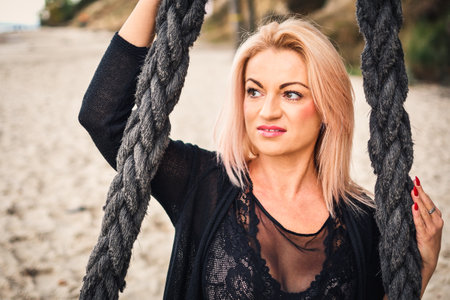 Session of a blonde-haired woman on a Polish beach. Girl on a swing on a sandy beach in Gdynia, Poland. Photo with a shallow depth of field.の写真素材