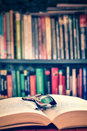 Open book and glasses with books on a shelf in the background. Theme of spending free time deepening your knowledge. Photo with a shallow depth of field.の写真素材