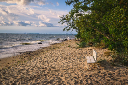 Beautiful seaside landscape on a summer holiday day. White bench on the beach with the waving sea in the background. Photo taken in Gdynia, Poland.の写真素材