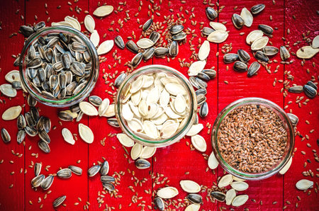 Sunflower, pumpkin and linseed seeds. Healthy food in glass jars on a red wooden table.