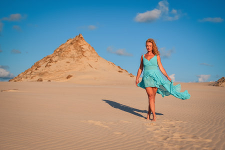 Beautiful blonde woman on hot sand with blue sky in the background. Photo taken on the shifting dunes over the Baltic Sea in Leba, Poland. Photo with a shallow depth of field with blurred background.の写真素材